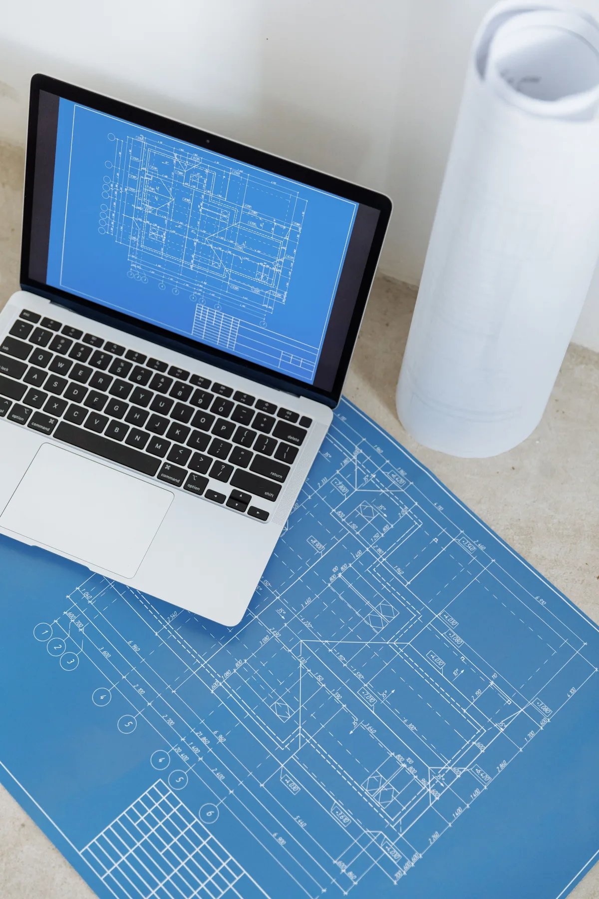 Laptop z cyfrowym rysunkiem technicznym obok drukowanych planów budynku